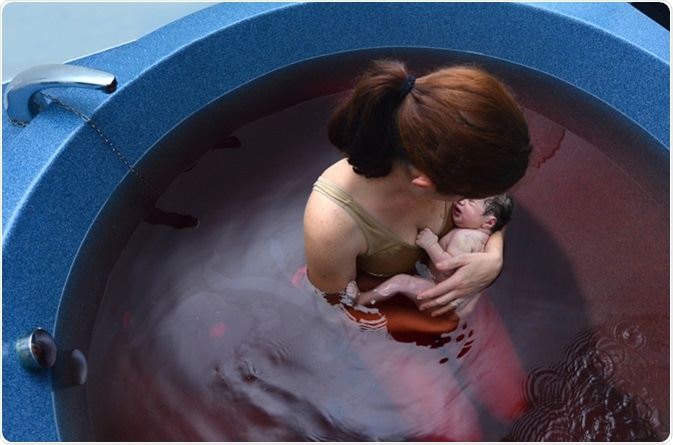 Young woman holds her baby in a pool after natural water birth. Image Credit: ChameleonsEye / Shutterstock
