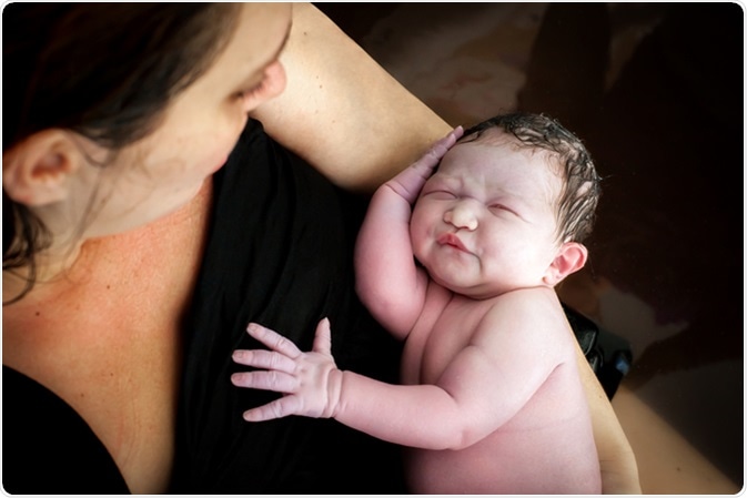 A woman holds her newborn son right after giving birth, they are still in the birthing pool after labor at home. Image Credit: In The Light Photography / Shutterstock