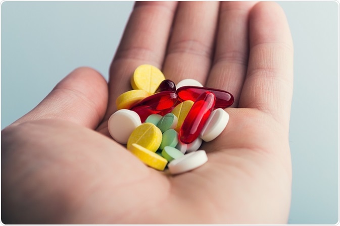Person holding out hand and holding several different types of pills.