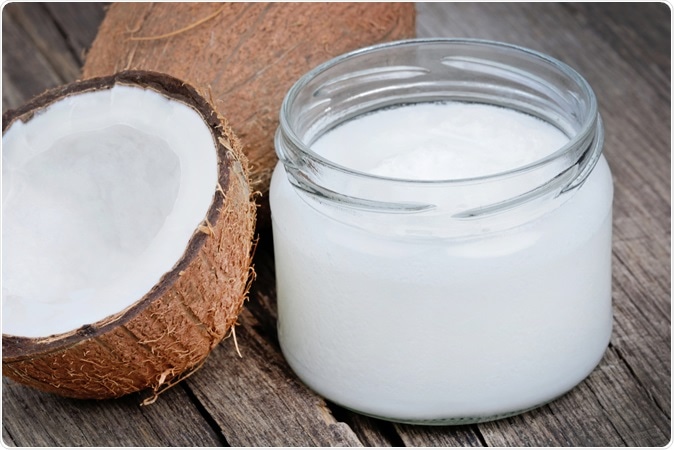 Coconut oil in a jar on wood table close-up. Image Credit: DeeaF / Shutterstock