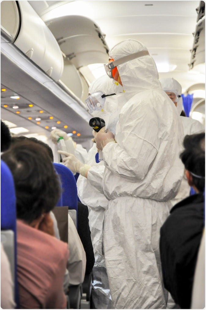 Medics in white hazmat protective suits checking and scanning passengers on a plane for Wuhan coronavirus. Image Credit: Delpixel / Shutterstock