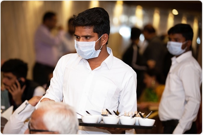 Jodhpur, Rajasthan, India - March 2020: Waiters wearing surgical masks serving food in a restaurant. Image Credit: Stockpexel / Shutterstock