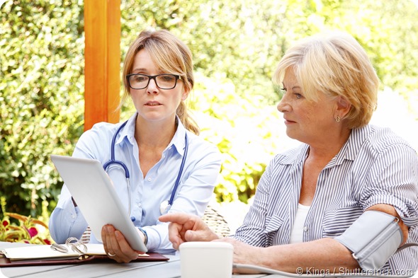 Elderly woman sitting in the garden with home health care nurse and consulting. Middle age caregiver holding in hand digital tablet and giving advice to her patient
