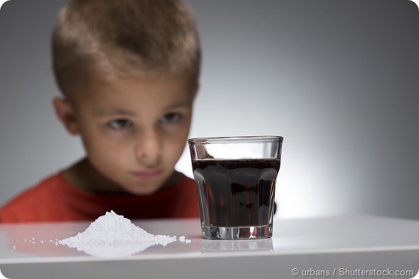 Young kid looks in front of sugar sweetened soft drink. The over-consumption of sugar-sweetened soft drinks is associated with obesity, type 2 diabetes, dental caries, and low nutrient levels