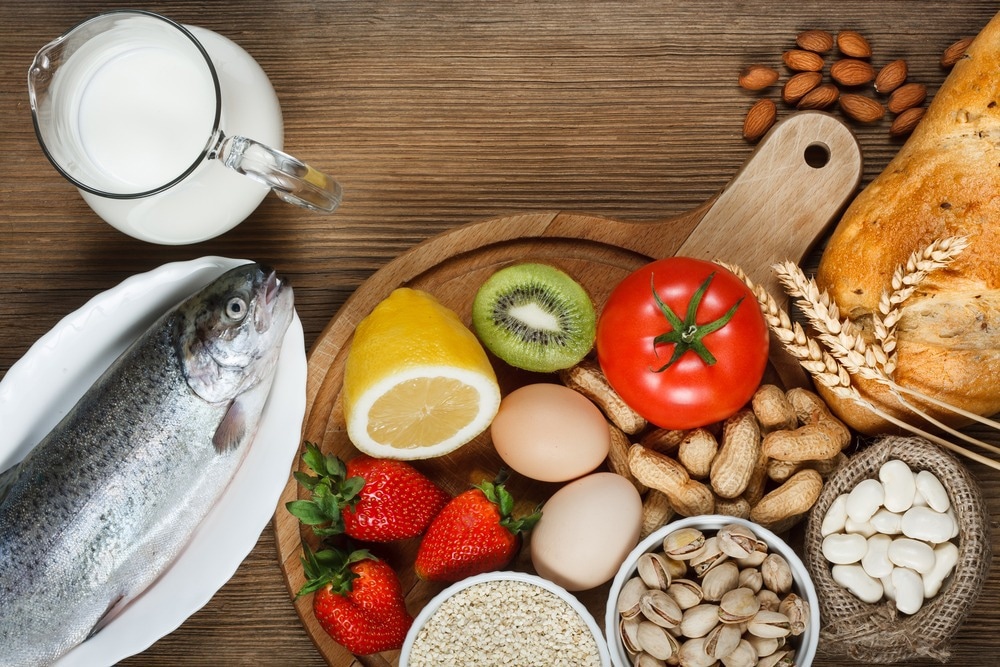 Allergy food concept. Allergy food as almonds, milk, pistachios, tomato, lemon, kiwi, trout, strawberry, bread, sesame seeds, eggs, peanuts and bean on wooden table. Image Credit: Evan Lorne/Shutterstock.com