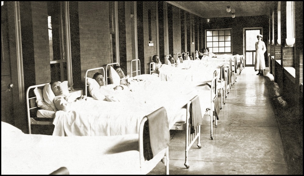 Vintage photo of a Hospital Hallway Lined With Men In Beds. Image Credit: chippix/Shutterstock.com