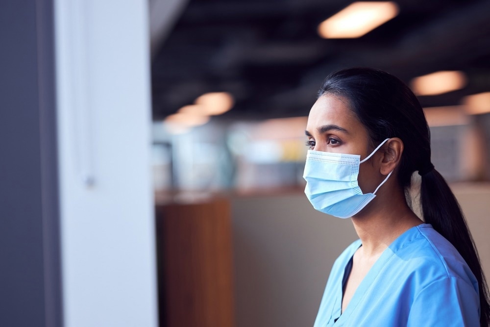 Female Doctor In Face Mask Wearing Scrubs Under Pressure In Busy Hospital During Health Pandemic. Image Credit: Southworks/Shutterstock.com